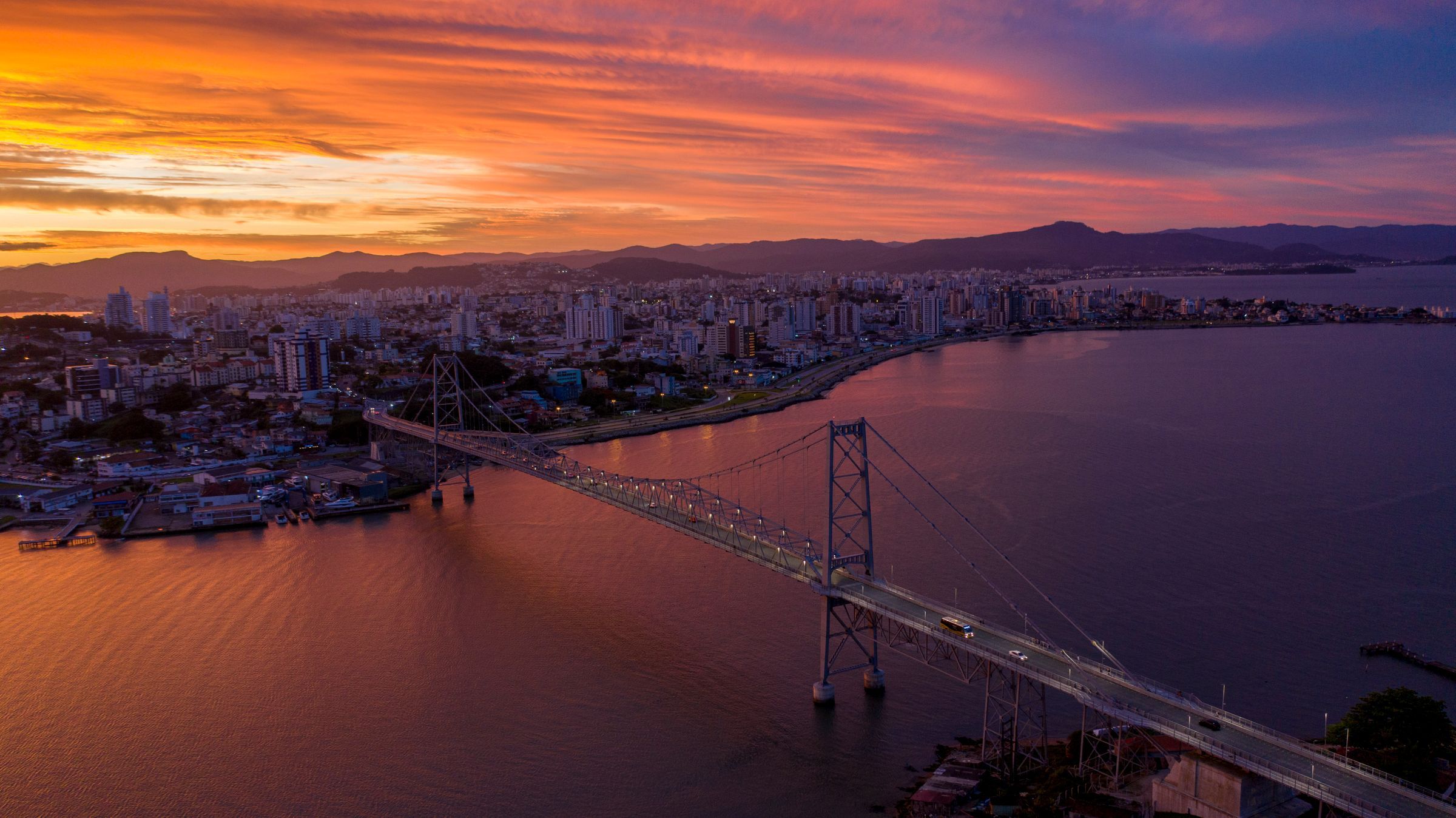 Vista aérea de Florianópolis ao pôr do sol, com a Ponte Hercílio Luz